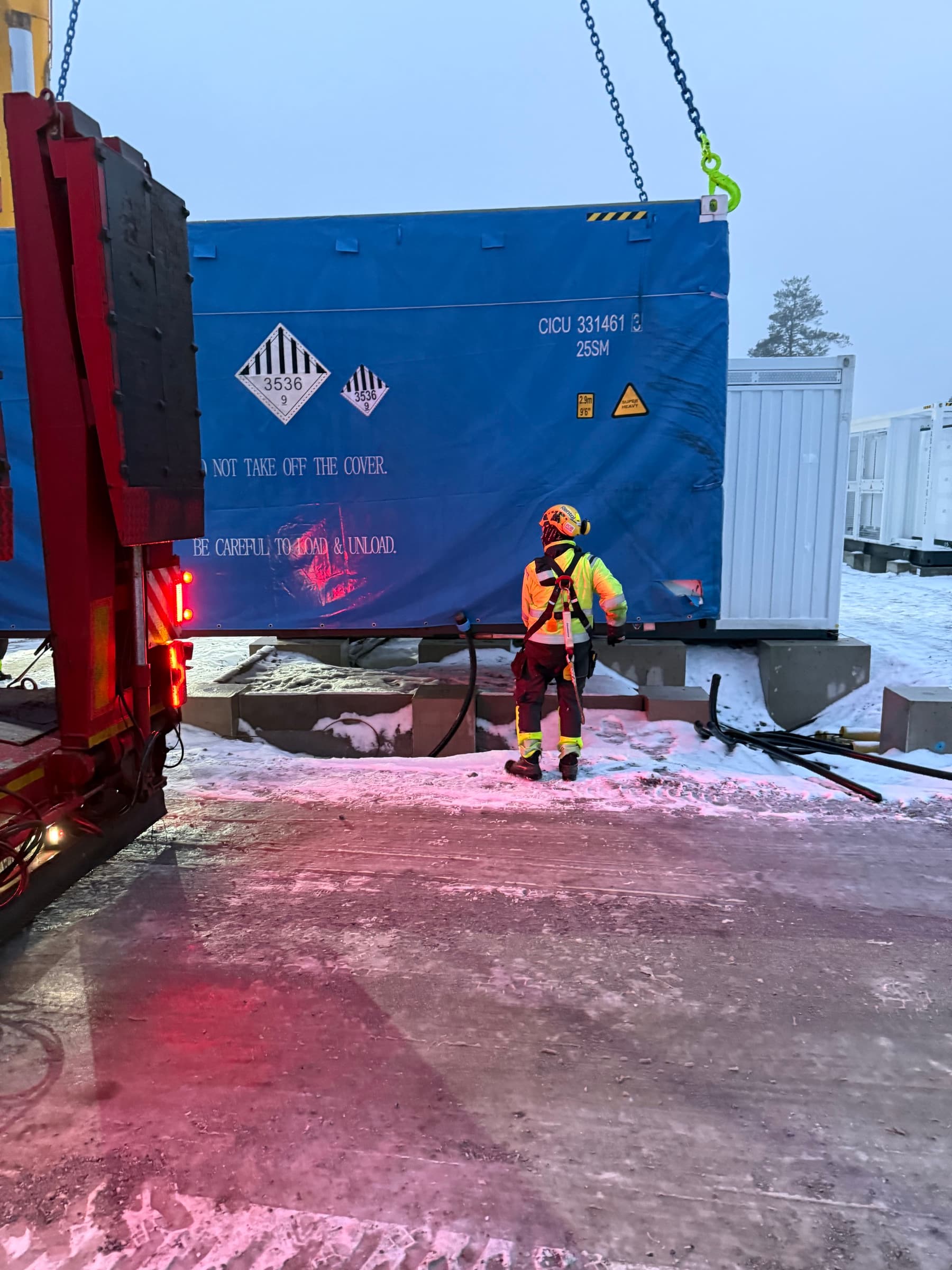 Battericontainer lossas från trailer i snö och kvällsljus