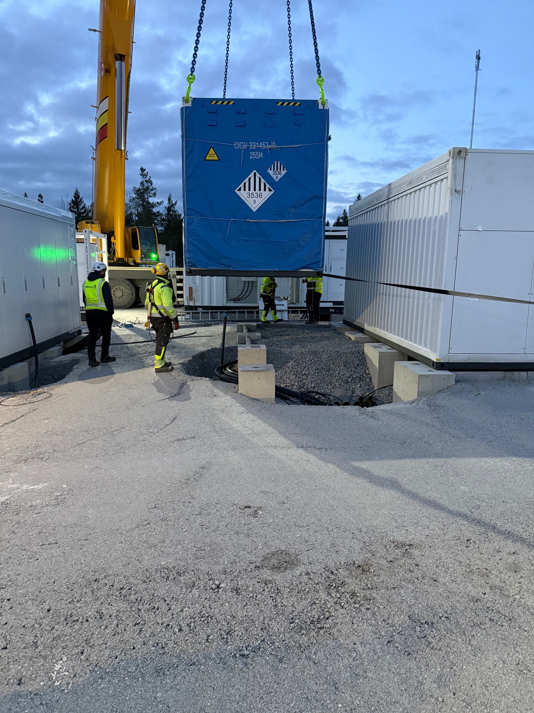 Battericontainer løftes af kran mens arbejdere overvåger