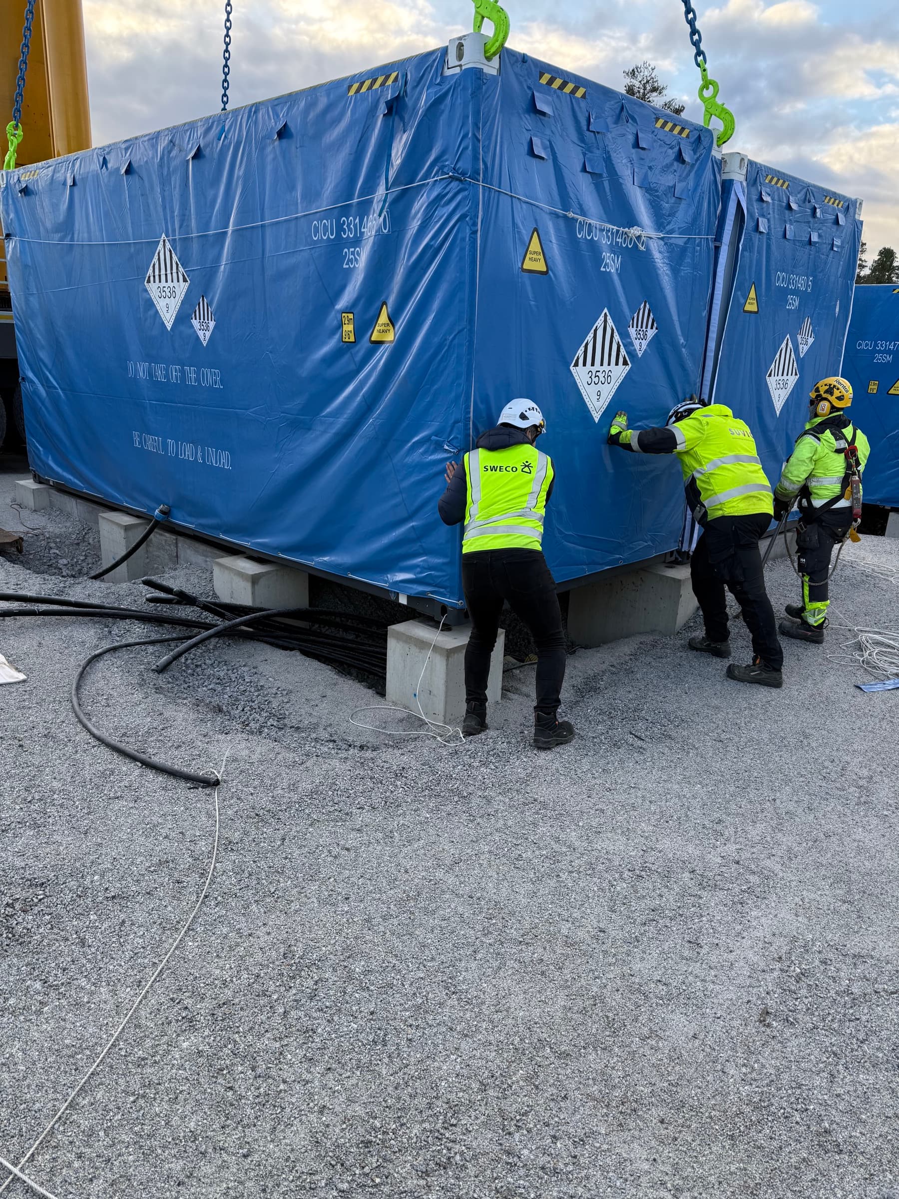 Arbetare guidar battericontainer på plats